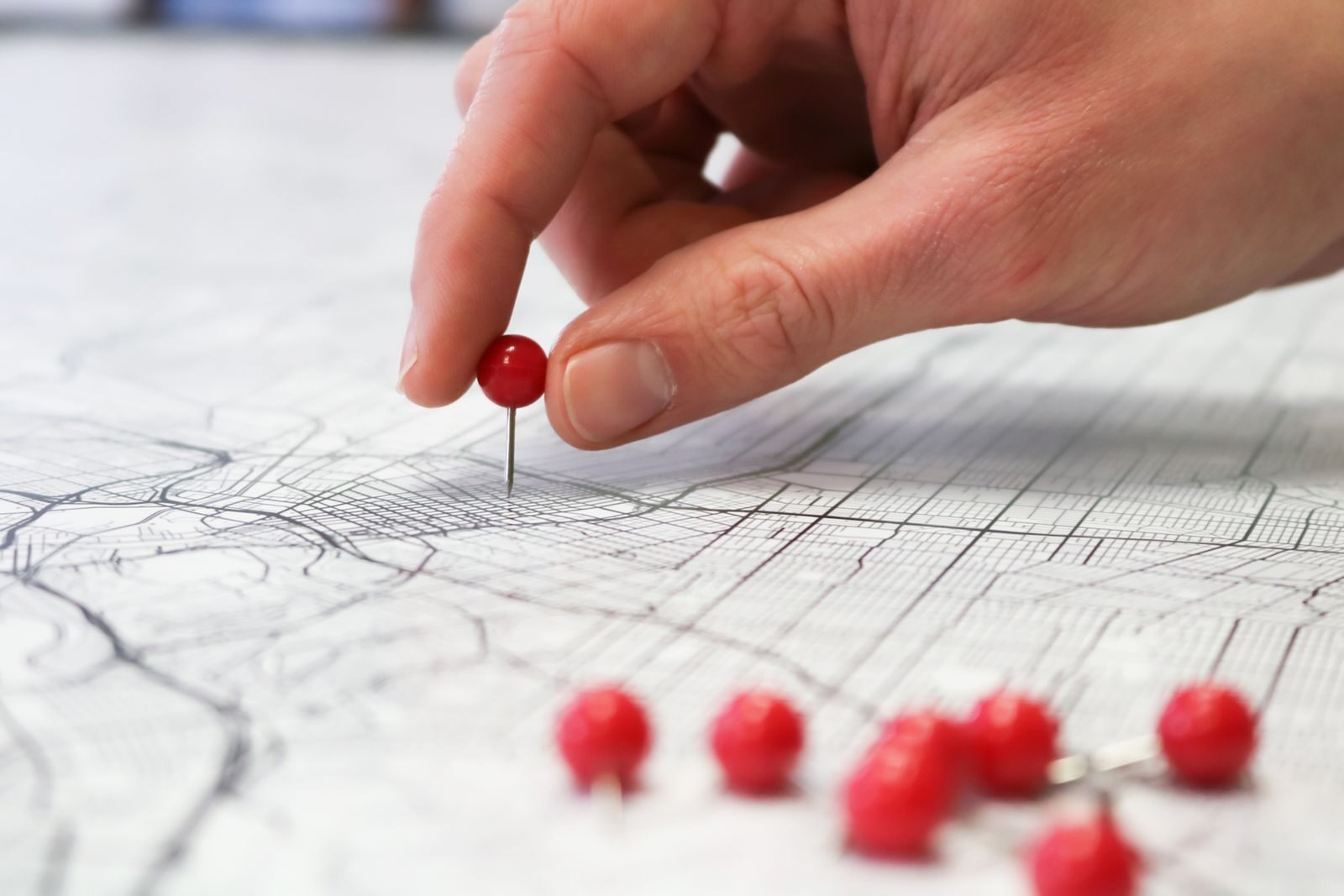 Photo by GeoJango Maps Close-up of a hand placing a red pin on a map indicating geographic location pinning.